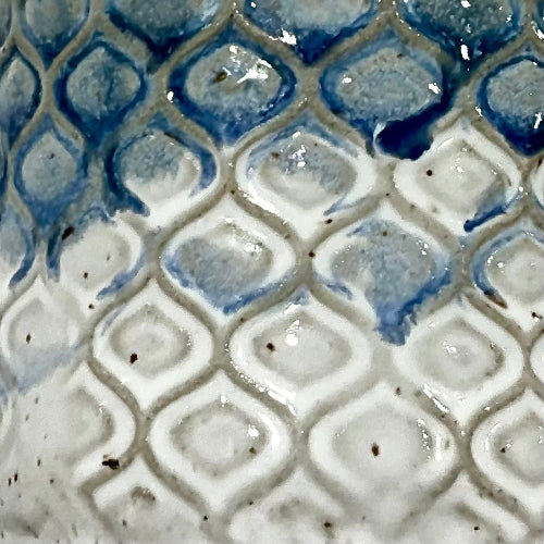 Close-up of a glossy ceramic surface with a repeating raised diamond pattern in white and blue glaze.